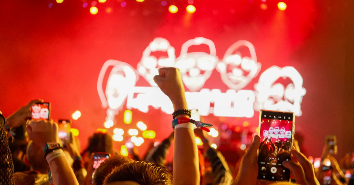 Vibrant concert atmosphere with fans capturing the stage on smartphones with raised hands.